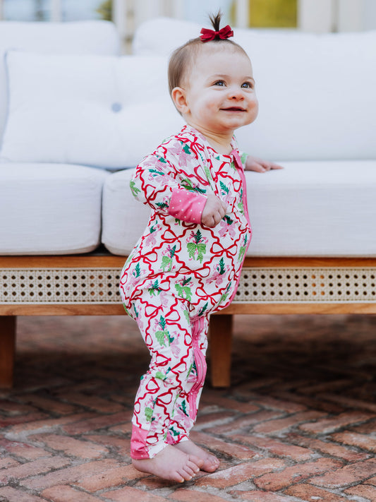 Baby standing up holding on to white couch smiling. Baby is wearing a colorful printed layette.