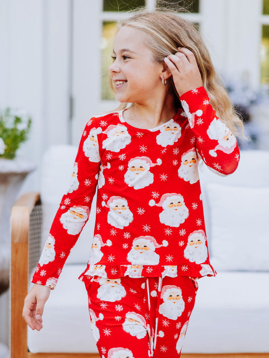 Girl tucking hair behind ear wearing a matching two piece set that is red with white Santa heads.