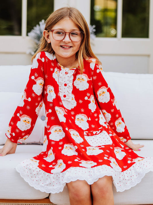 Girl sitting outside on white couch wearing a red santa printed dress.