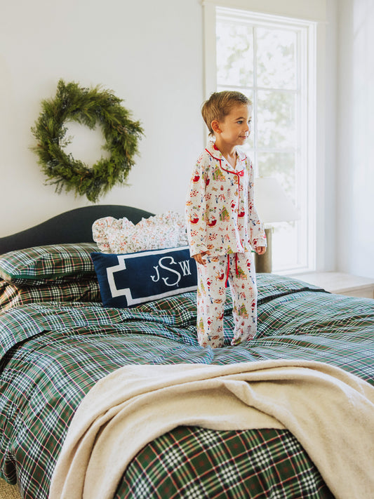 Boy standing in the middle of a traditional green plaid made bed. Throw blanket at corner of bed.