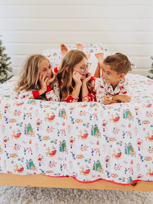 Three children laying on Christmas bedding bed.