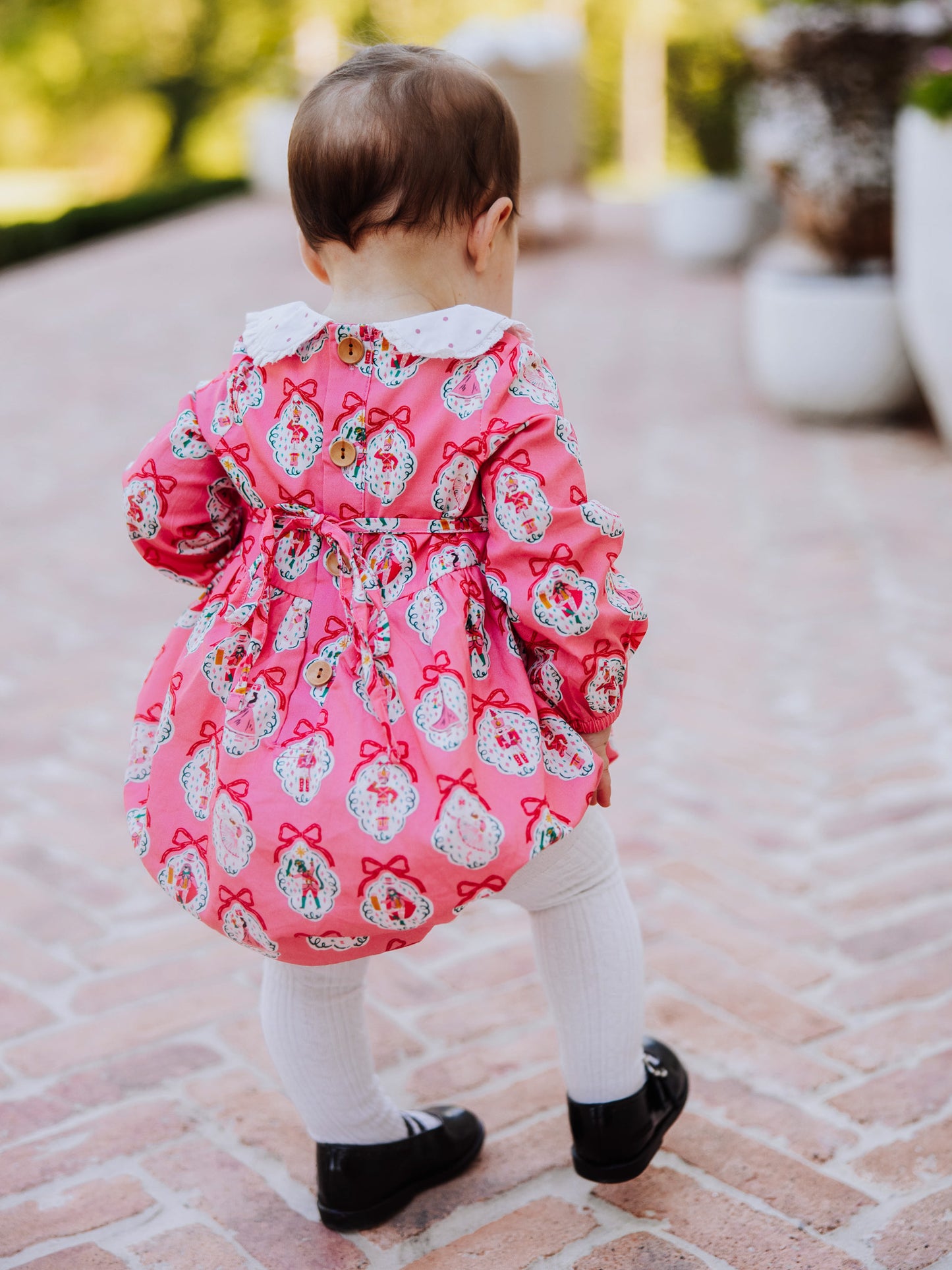 Baby girl outside wearing apink nutcracker print classic bubble with white tights and black mary janes.