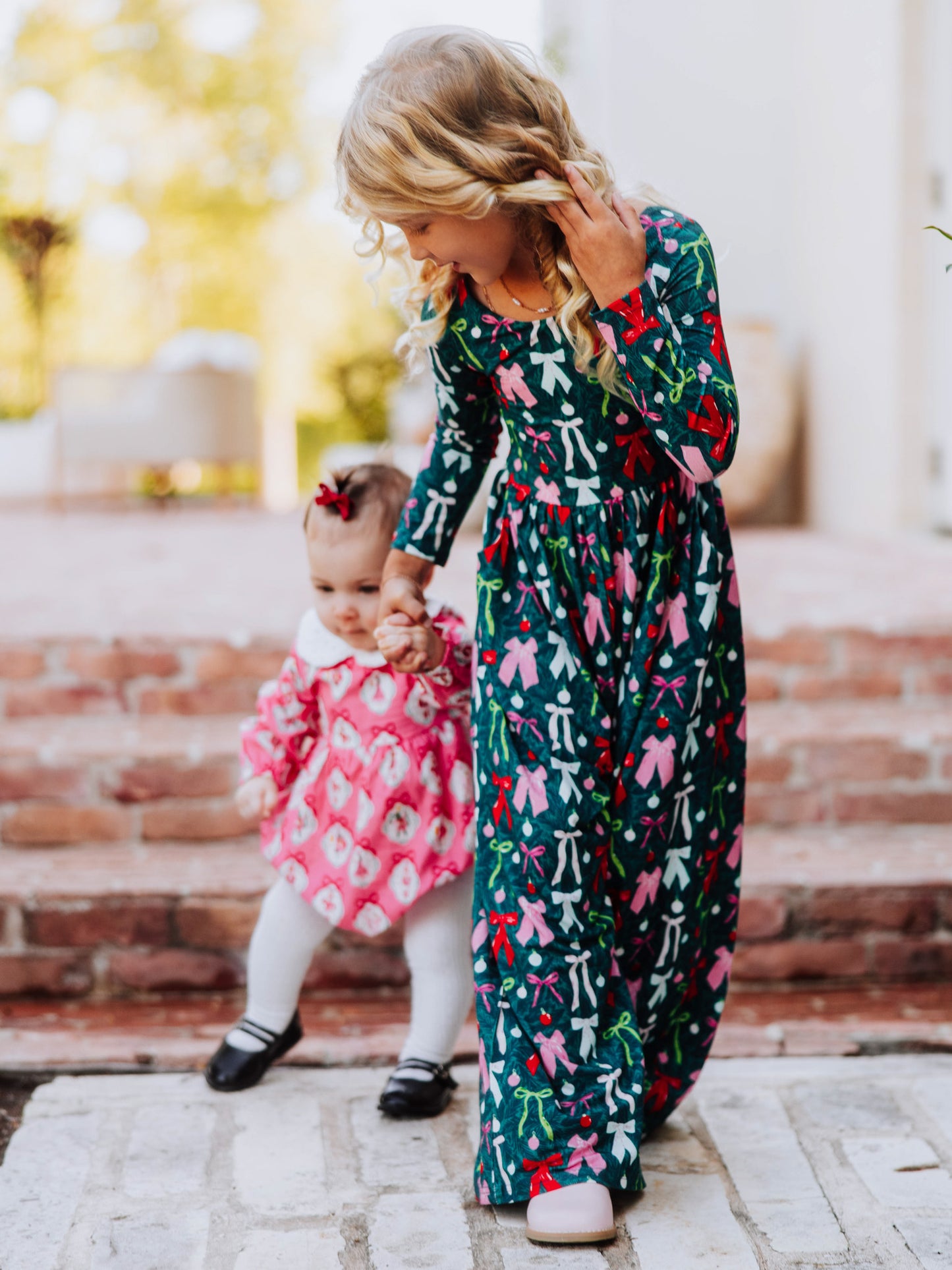 Two girls holding hands walking. One is wearing a classic bubble and the other is wearing a bow printed leggy romper.