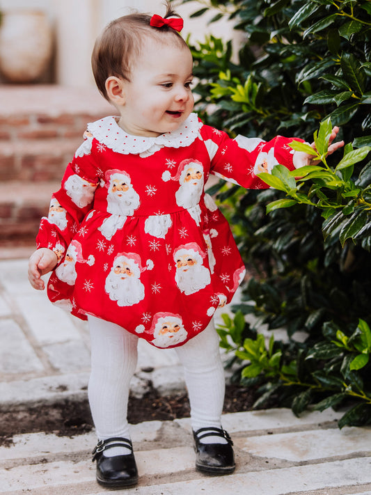 Baby girl outside wearing a jolly santa print classic bubble with white tights and black mary janes.