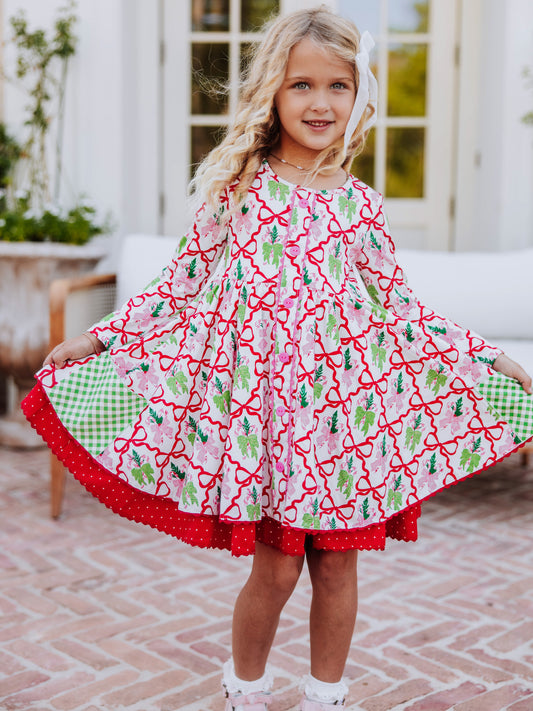 Girl standing outside holding both sides of dress. Dress is a holiday bow printed pattern with double layers.
