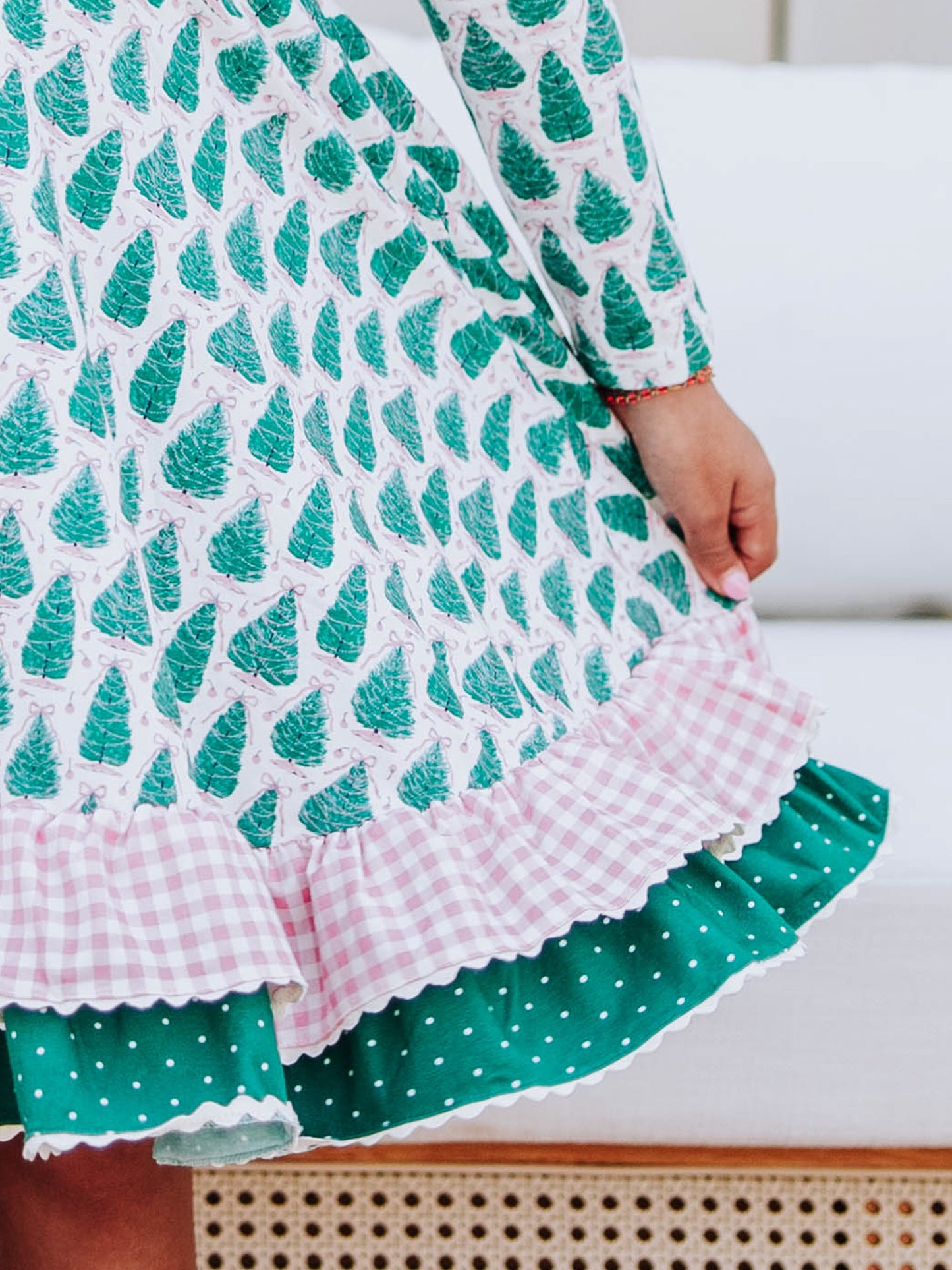 Up close shot of girl holding out the side of her Christmas tree themed dress that has double ruffles and ric rac trim