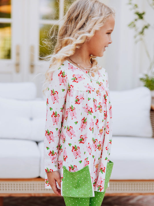 Girl standing outside in front of couch wearing a holiday themed top with green leggings with white polka dots that have ruffles at bottom.