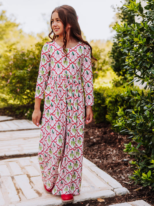 Girl wearing a holiday bow themed leggy romper outside near a bush