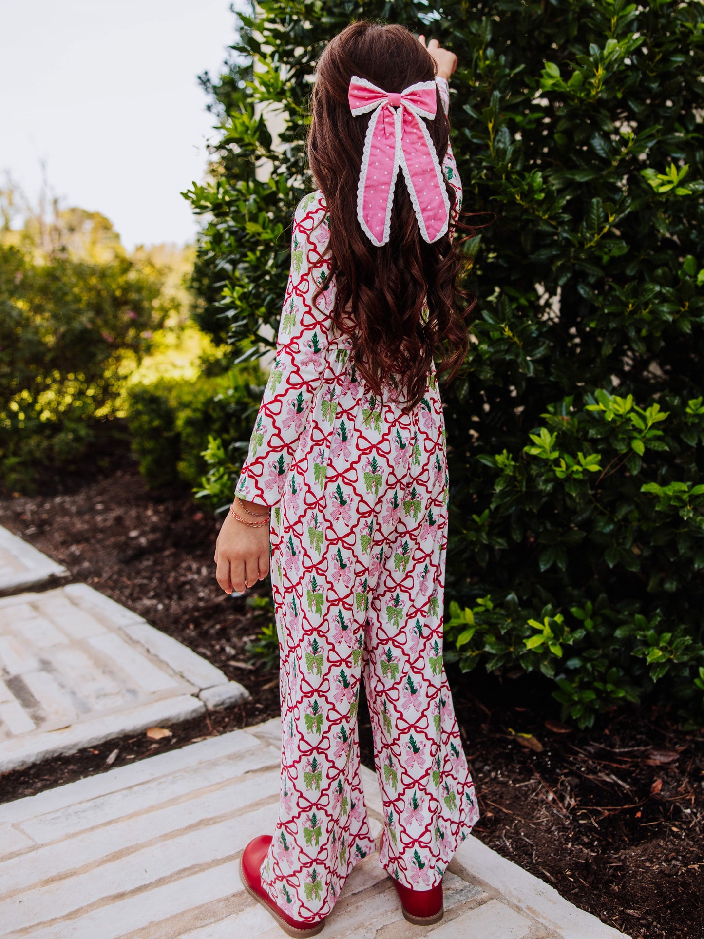 Girl wearing a holiday bow printed leggy romper looking at bush