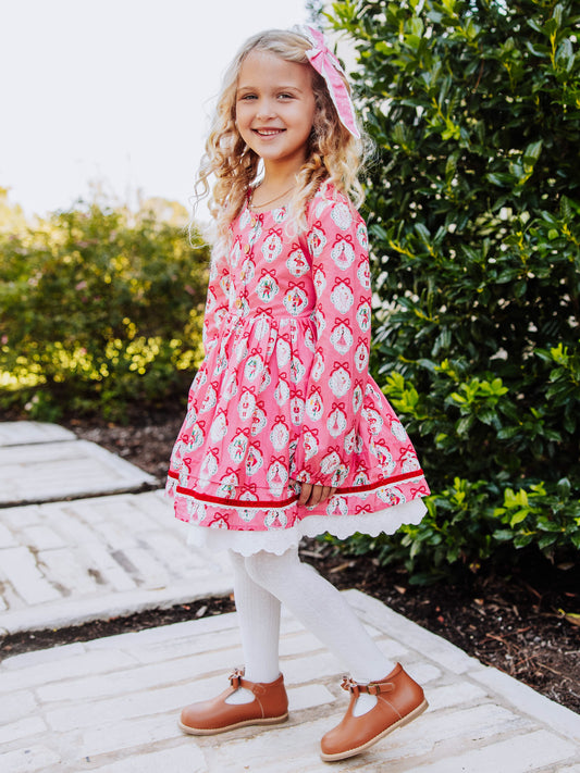 Girl standing outside next to greenery wearing a pink holiday themed dress.