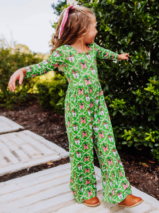 Model wearing a green bow printed leggy romper and is holding arms out to the side.