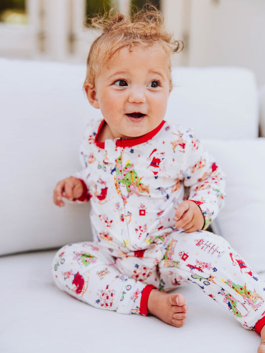 Baby girl sitting on couch wearing a north pole printed holiday layette.