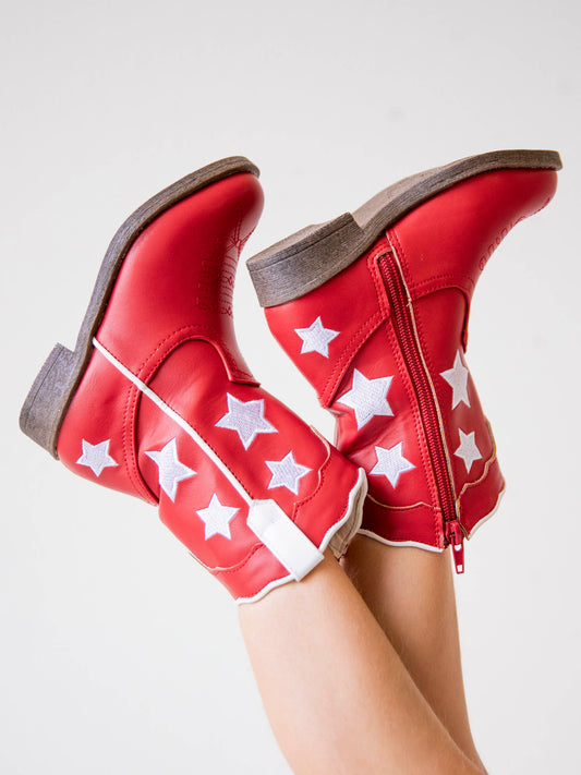 Picture of girl wearing red boots with white stars, white pull tabs, and a side zipper. Soles are brown.