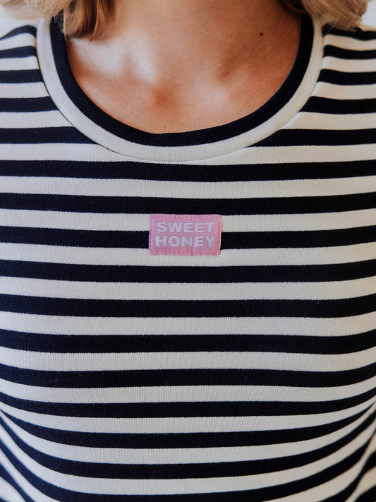 Close up of navy and ivory colored shirt that has a pink and white stitched sweethoney logo tag at center of chest.
