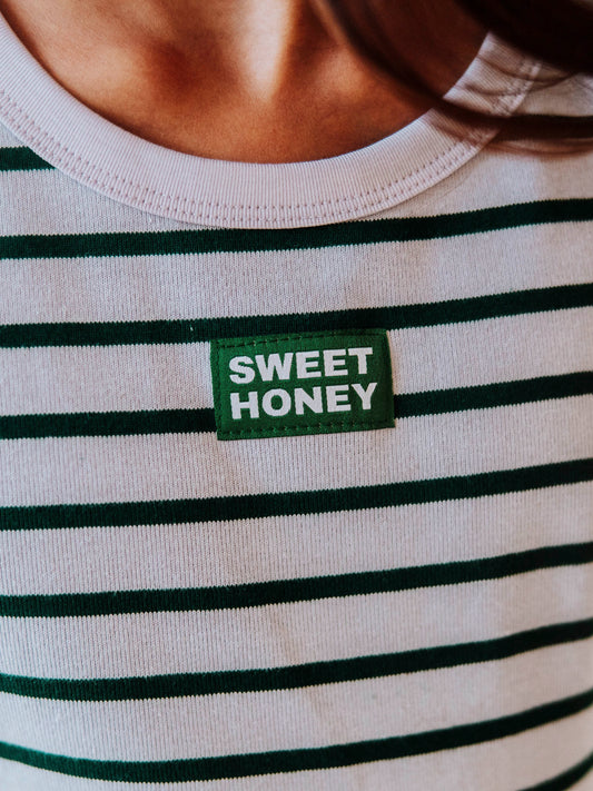 Up close shot of a SweetHoney logo tag that is green and white in color. Color of shirt is green and gray overall.