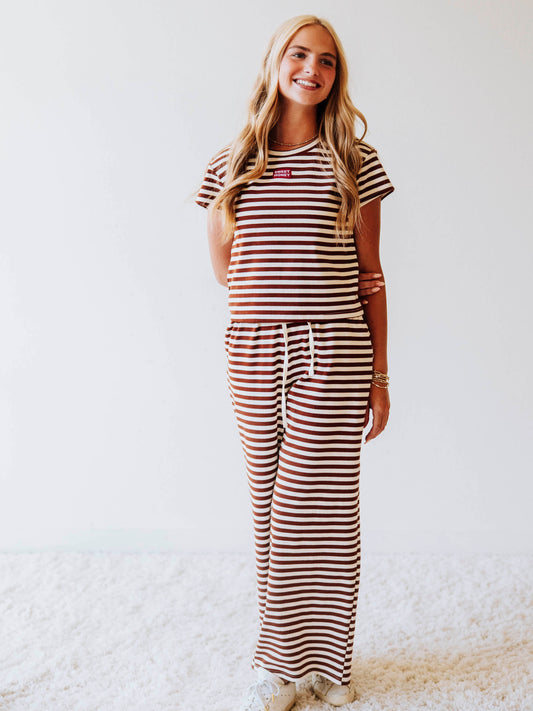 Model is wearing a chocolate and ivory striped, two piece pant set. Top has a SweetHoney logo tag stitched at chest