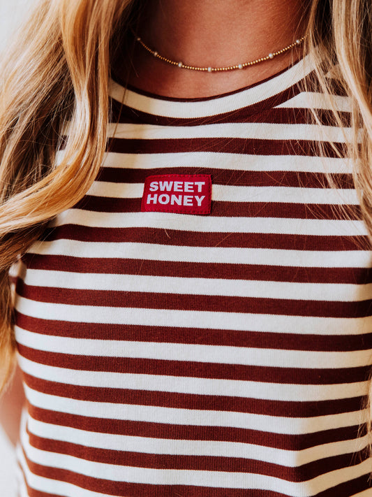 Model is wearing a chocolate and ivory striped, two piece pant set. Top has a SweetHoney logo tag stitched at chest. Pic is a close up of tag