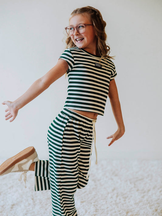 Girl is wearing a two-piece hunter green and ivory striped pant set. Girl is wearing tan shoes and is posing.