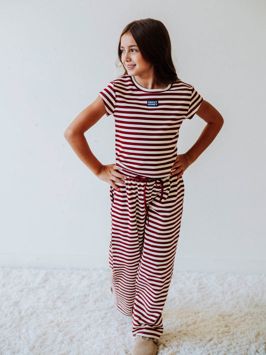 Girl is wearing a two-piece red and ivory striped pant set. Girl is wearing tan clogs and is posing.