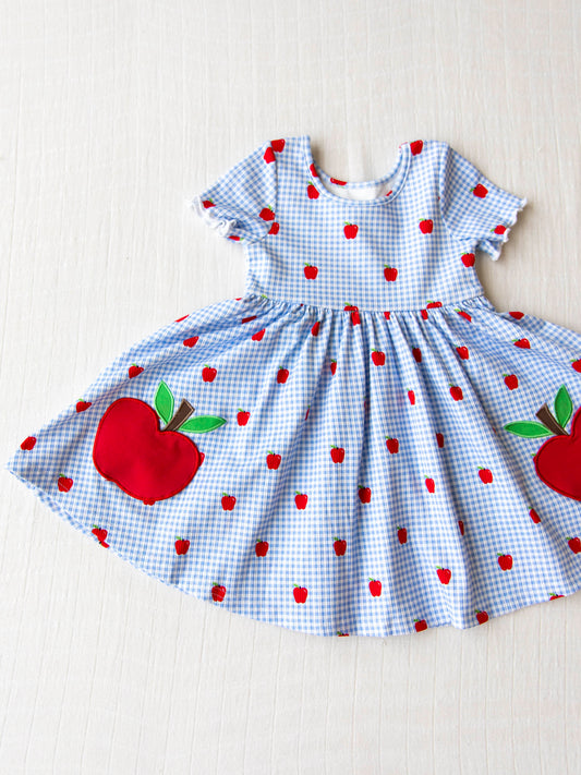 Flat lay of blue apple gingham dress with two big apples at bottom
