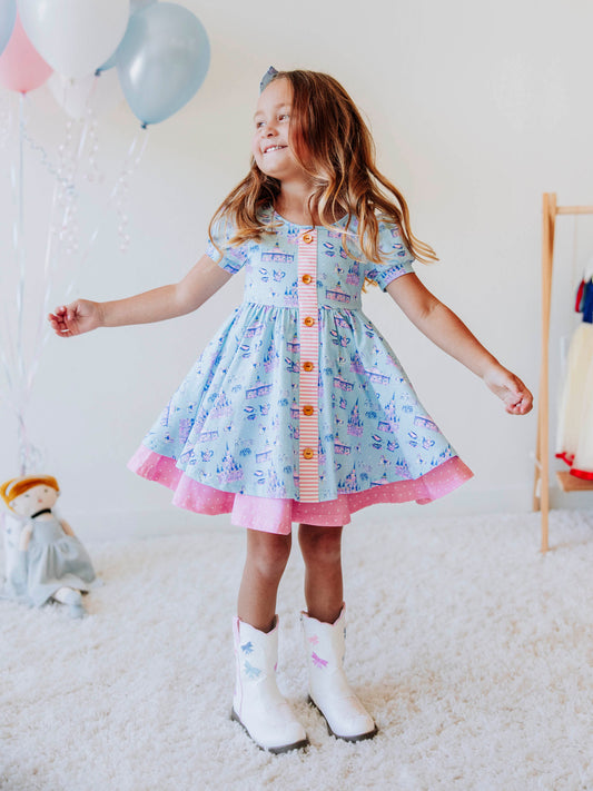 Bring a little fairytale charm to her day with our Most Magical Prim Dress! This enchanting dress features our exclusive Most Magical print — a whimsical pattern filled with castles, teacups, and dreamy pastel details. Designed with a sweet button-down front, short puff sleeves, and a full twirl skirt trimmed in pink polka dots, it’s perfect for playdates, park adventures, and magical memories.