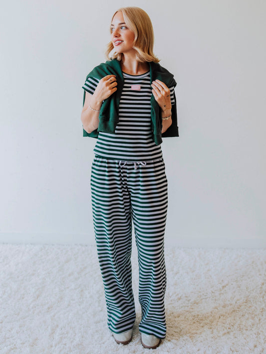 Model is wearing a green and lavender striped two-piece set with a green sweater draped over her shoulder.