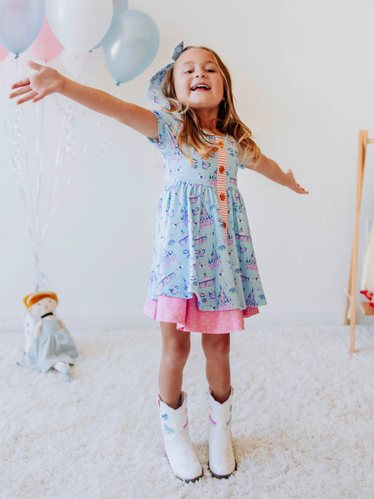 Bring a little fairytale charm to her day with our Most Magical Prim Dress! This enchanting dress features our exclusive Most Magical print — a whimsical pattern filled with castles, teacups, and dreamy pastel details. Designed with a sweet button-down front, short puff sleeves, and a full twirl skirt trimmed in pink polka dots, it’s perfect for playdates, park adventures, and magical memories.