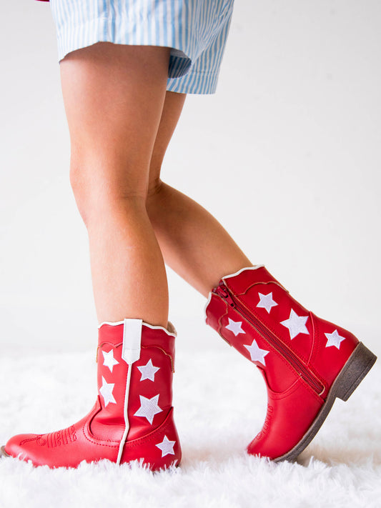 Picture of girl wearing red boots with white stars, white pull tabs, and a side zipper. Soles are brown.