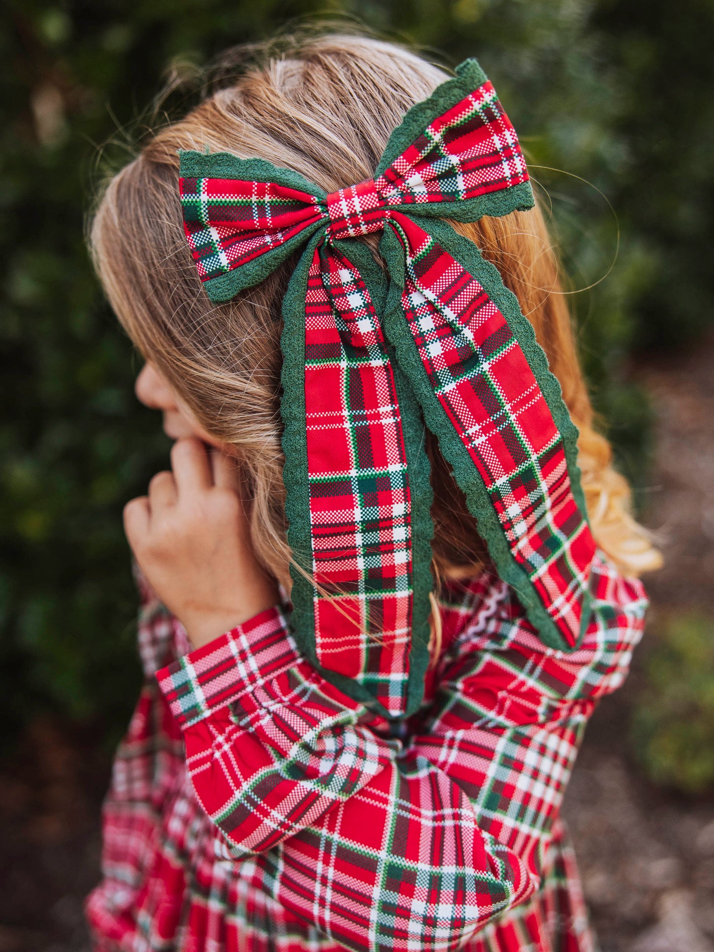 Girl outside wearing a red traditional Christmas colored bow trimmed in green dainty lace. Girl is wearing same colored outfit as bow.