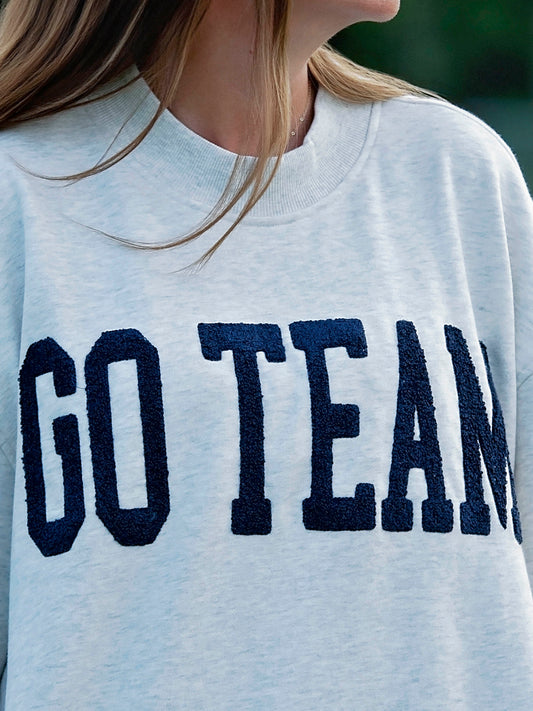 Close up of Women outside wearing a heathered gray sweater that says GO TEAM in a deep navy color