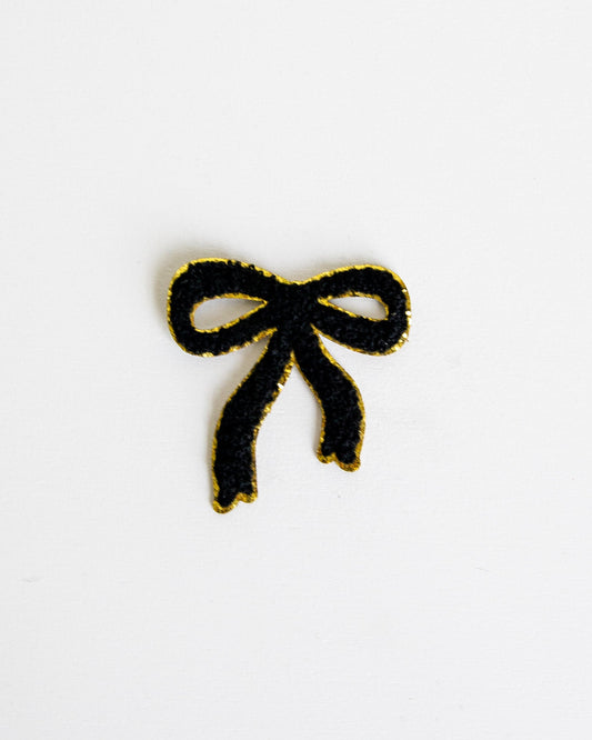 A small black bow-shaped patch with a gold metallic outline, centered on a plain white background.