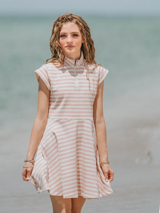 Model outside on a beach looking at the camera and wearing a dove pink and ivory striped dress.