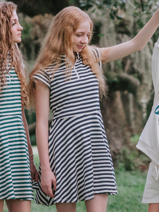 Group of girls outside. Two of them are in the same style dress. One dress is hunter green and ivory striped and the other is navy and ivory striped.