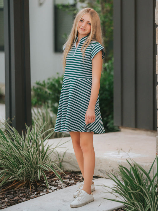 Model is outside on porch wearing a lavender and green stiped dress with white canvas shoes.