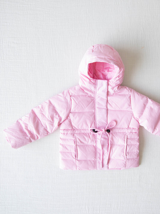 Keep her cozy and cute all season long in our Pink Puffer Jacket — the perfect blend of warmth and style! This soft, quilted jacket features a full zipper closure with a button placket, ensuring extra protection from chilly winds. Hidden front pockets keep little hands warm (or treasures tucked away), while the adjustable waist toggle allows for the perfect, comfortable fit. Designed in a beautiful blush pink hue, this girls’ puffer jacket pairs effortlessly with any winter outfit for a look that's fun!