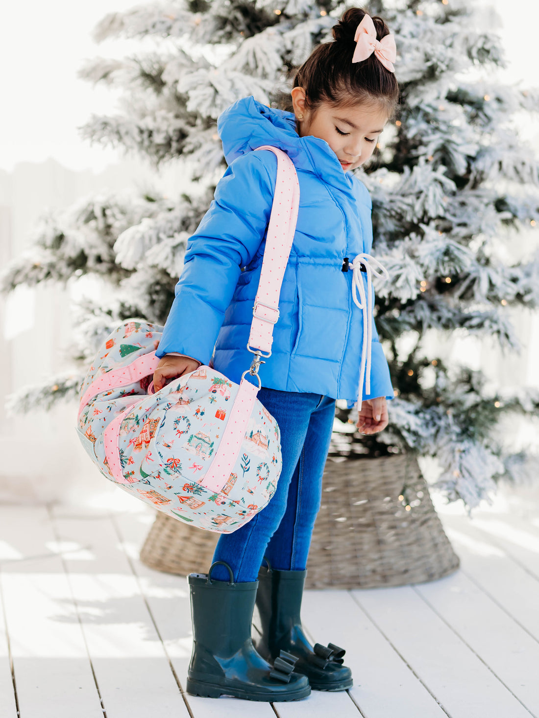 Little girl wearing our Puffer Jacket - Sapphire Blue & Cheery Rain Boot - Forest Green, while carrying our Everyday Duffle - Christmas Village