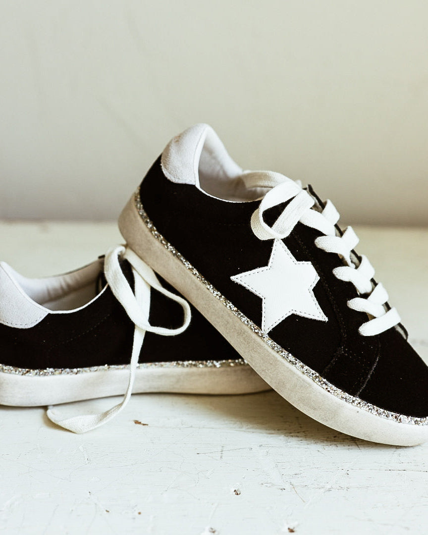 Black suede shoe with white star and glitter accents around shoe