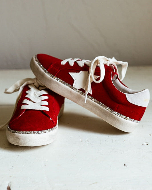 Pair of red suede tennis shoes with a white canvas star on the side with silver glitter trim around shoe