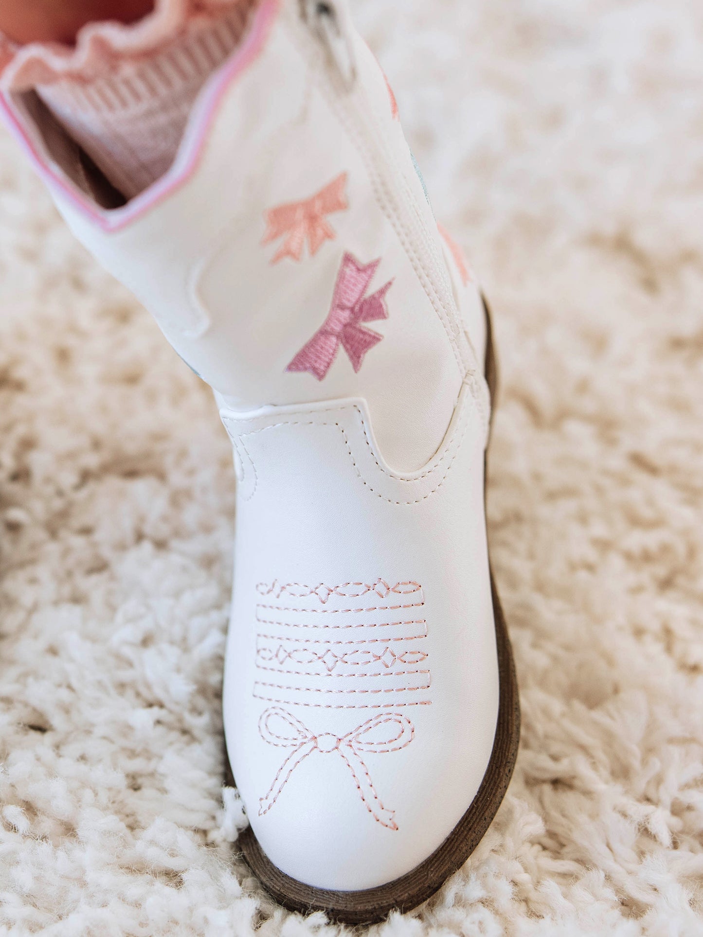Step into sweetness with our Girls Bow Paneled Cowboy Boots, designed for twirls, giggles, and all-day play. These white faux-leather boots feature pastel pink, blue, and lavender star embroidery, charming bow panels, and an easy side zipper closure for quick on-and-off. With a soft interior lining and sturdy sole, these girls’ Western boots perfectly blend comfort and style—ideal for everyday wear, special occasions, or matching with her favorite SweetHoney dress.