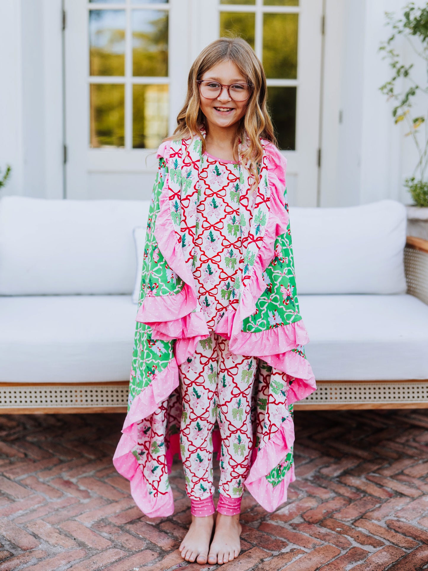 Model is wearing a matching set of colorful red bow printed pajamas and has a matching blanket wrapped around her. 