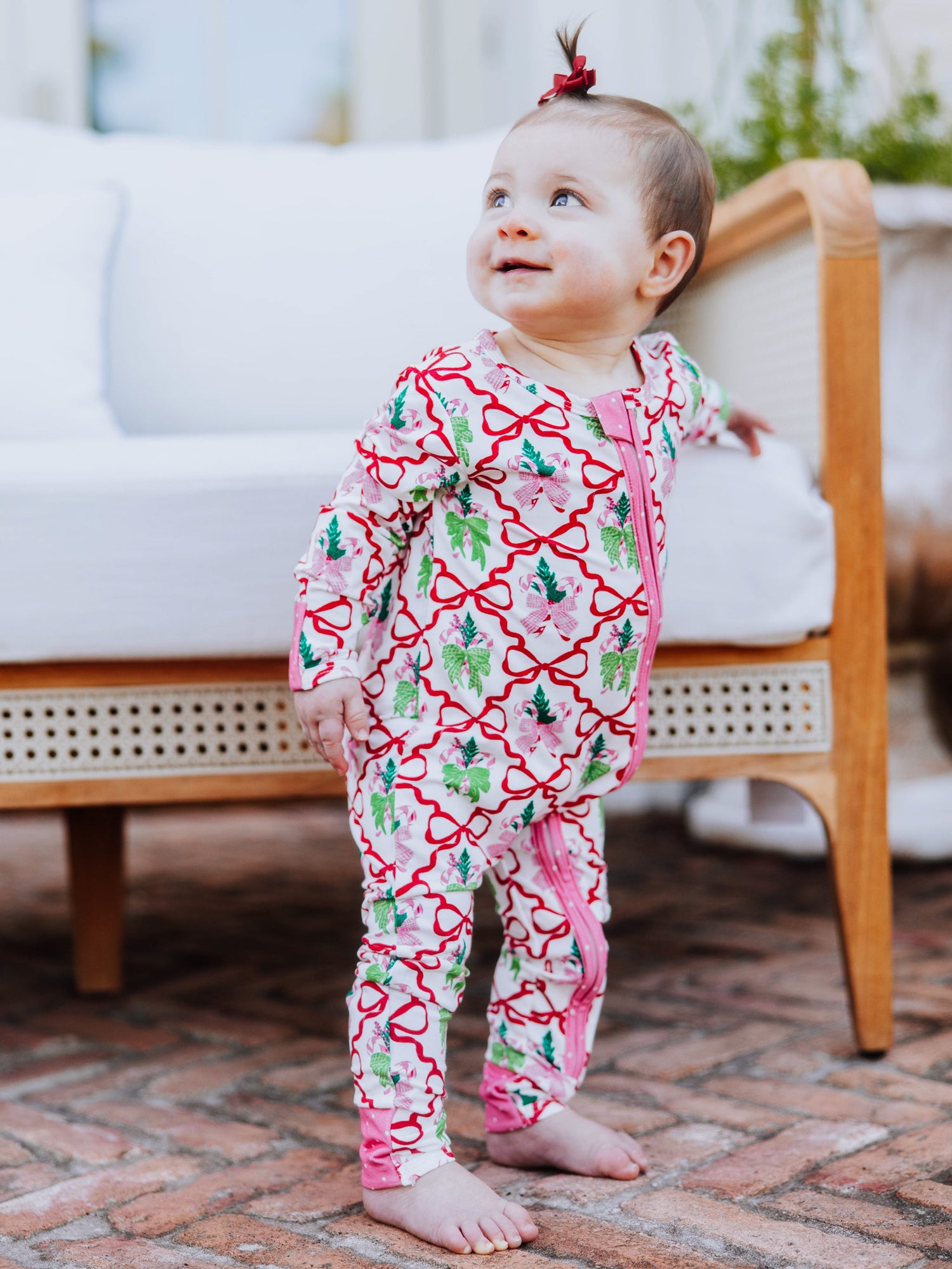 Baby standing up holding on to white couch smiling. Baby is wearing a colorful printed layette. 