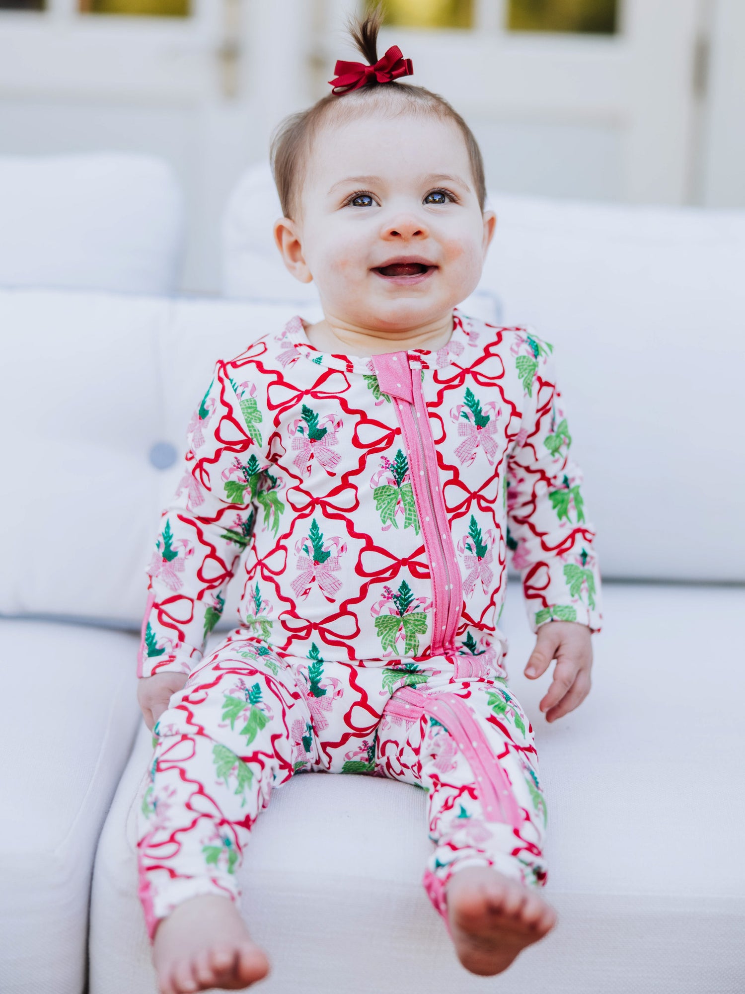 baby is sitting down on white couch smiling. Baby is wearing a colorful printed layette. 