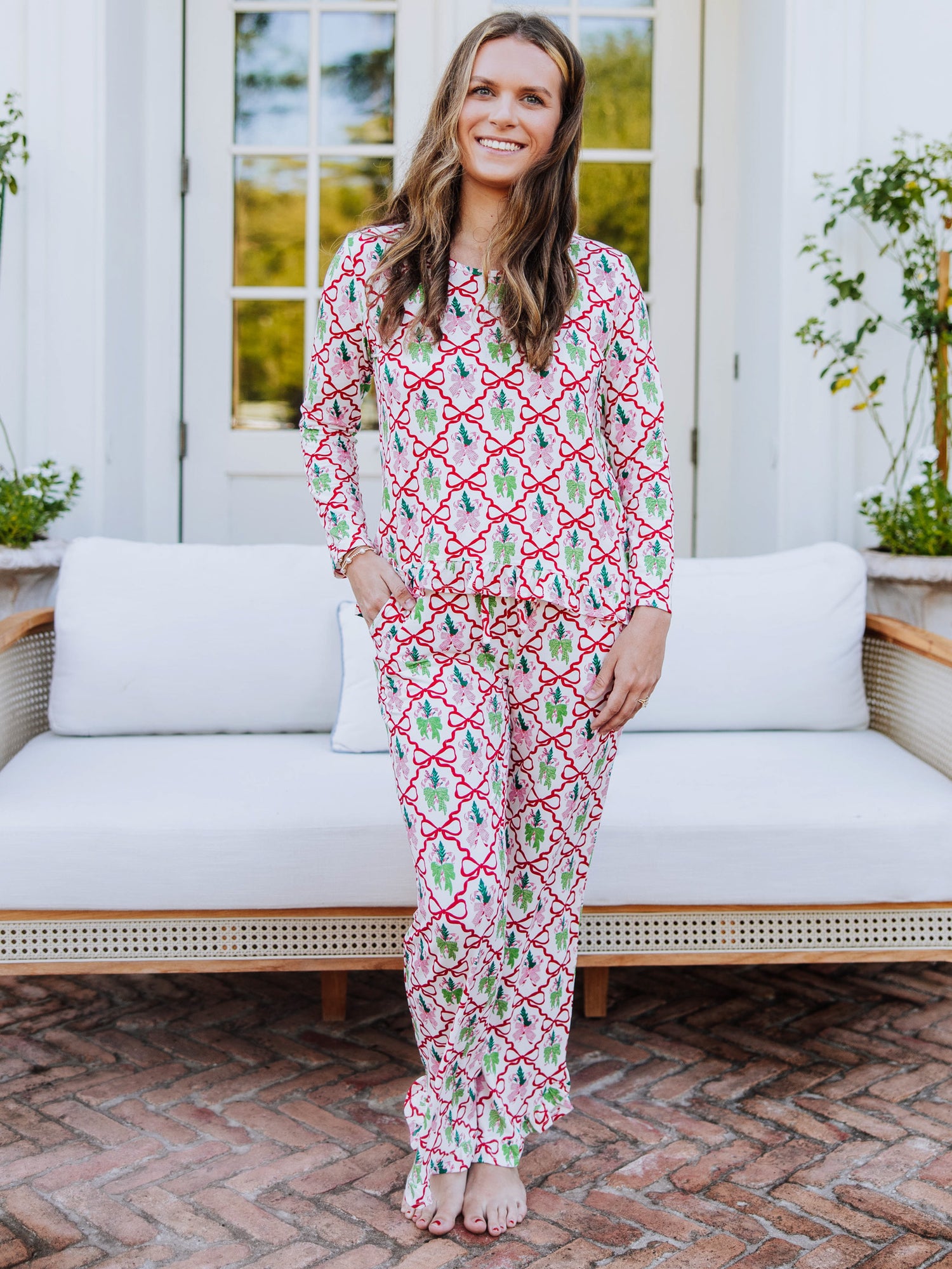Women standing outside in front of couch wearing a matching ruffled pant set that has many different colorful bows on it. 
