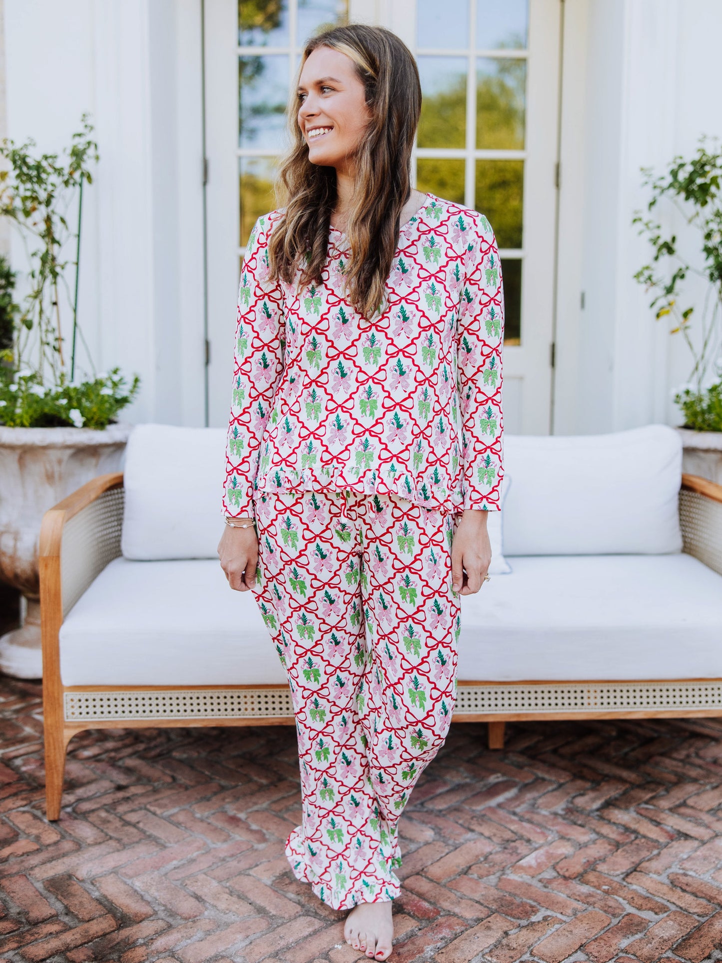 Women standing outside in front of couch wearing a matching ruffled pant set that has many different colorful bows on it. 