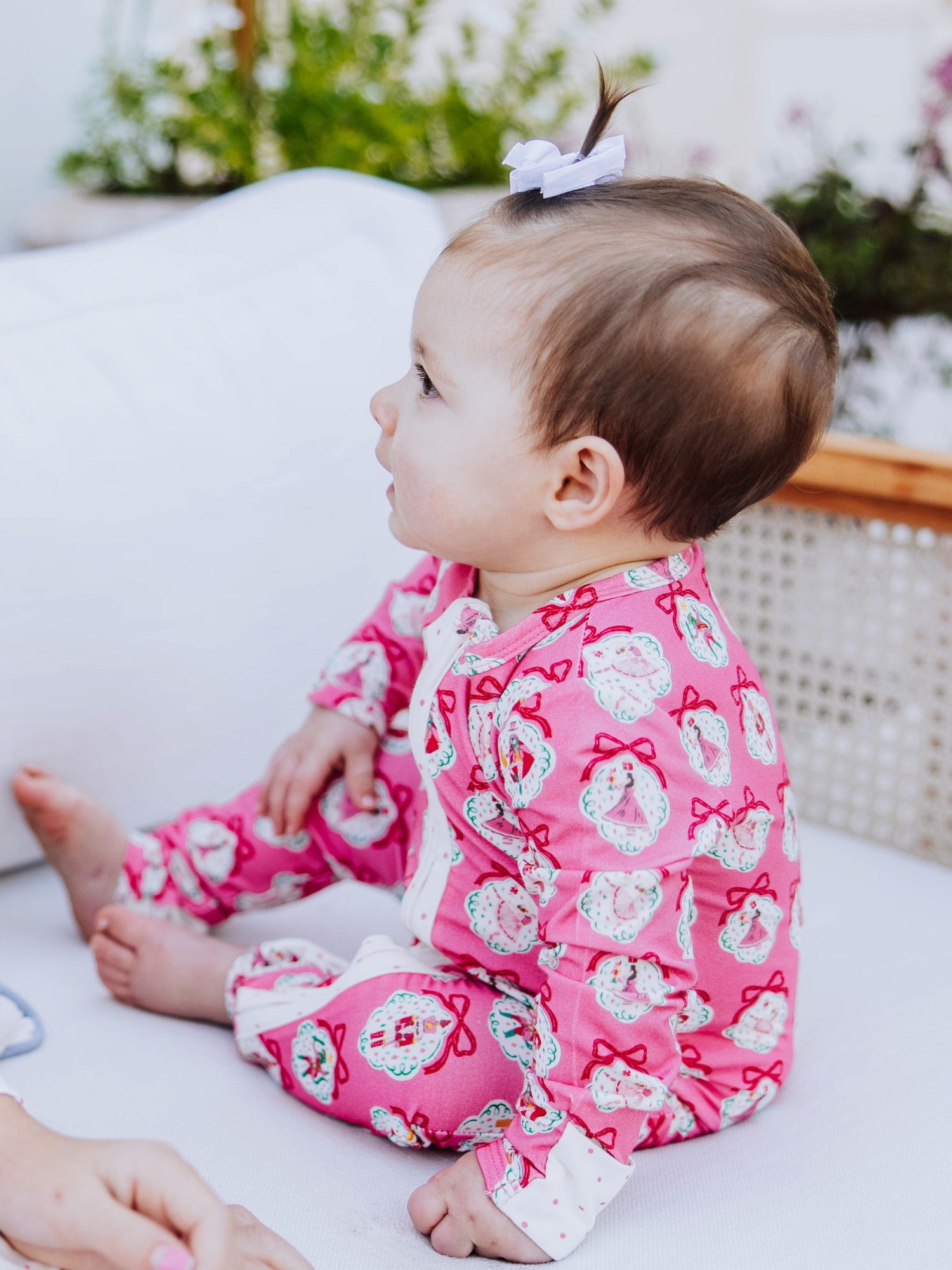 Baby sitting on white couch wearing a pink nutcracker printed layette. 