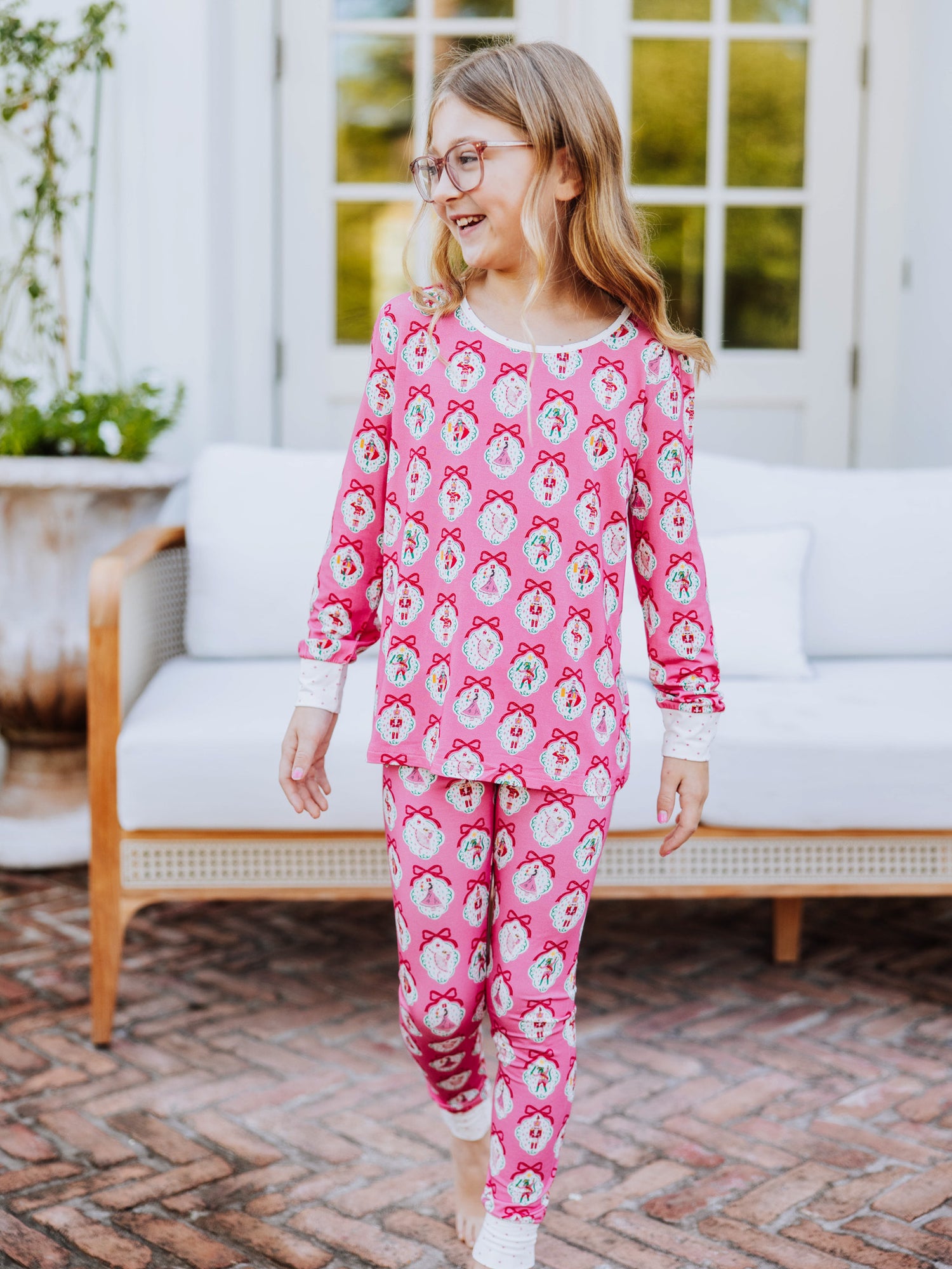 Girl walking outside on brick steps and is wearing a matching pair of fitted pajamas that have a pink nutcracker print on them. 