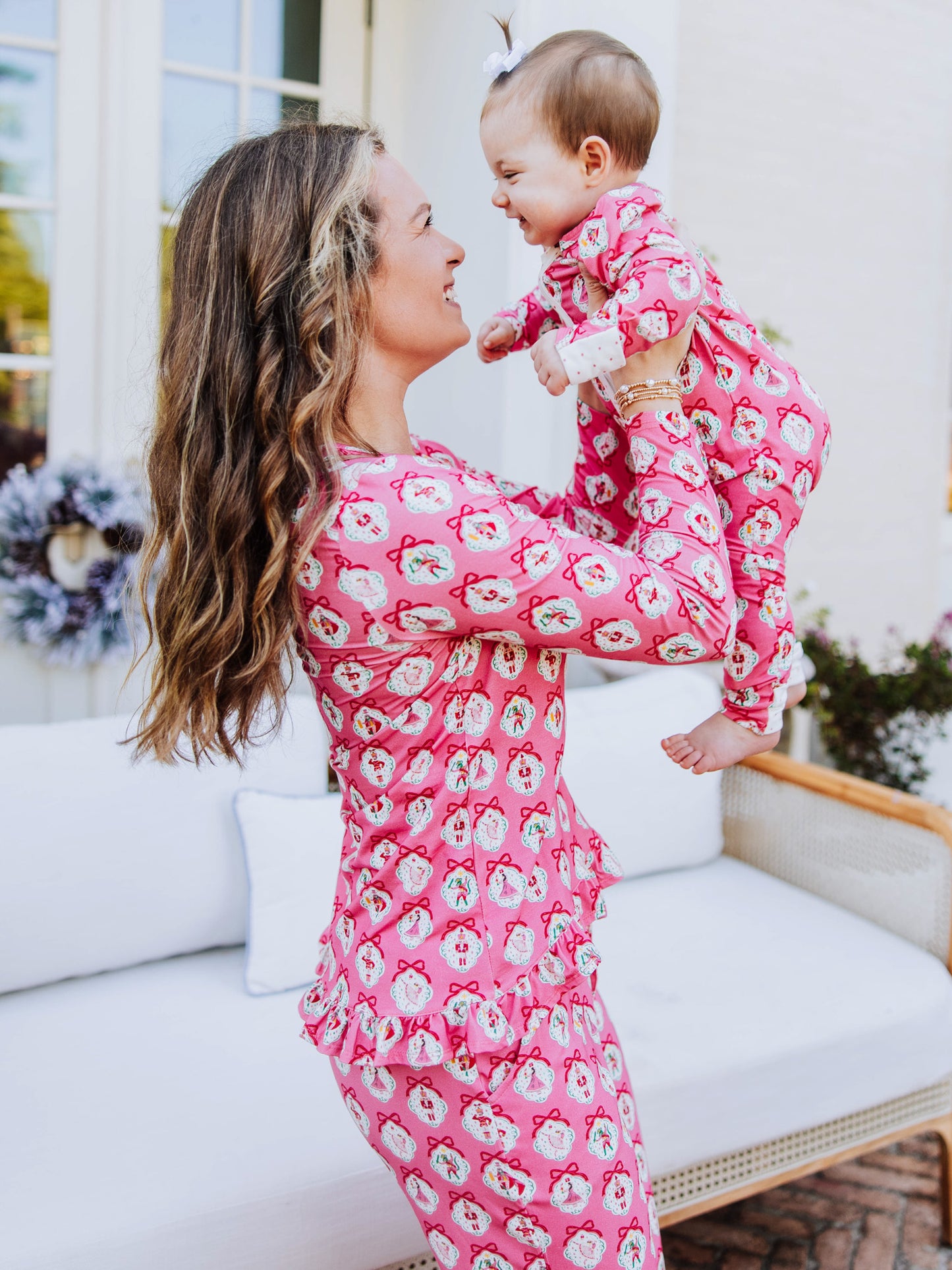 Mom holding up baby and both are wearing the same matching printed pajamas. Pink nutcracker.