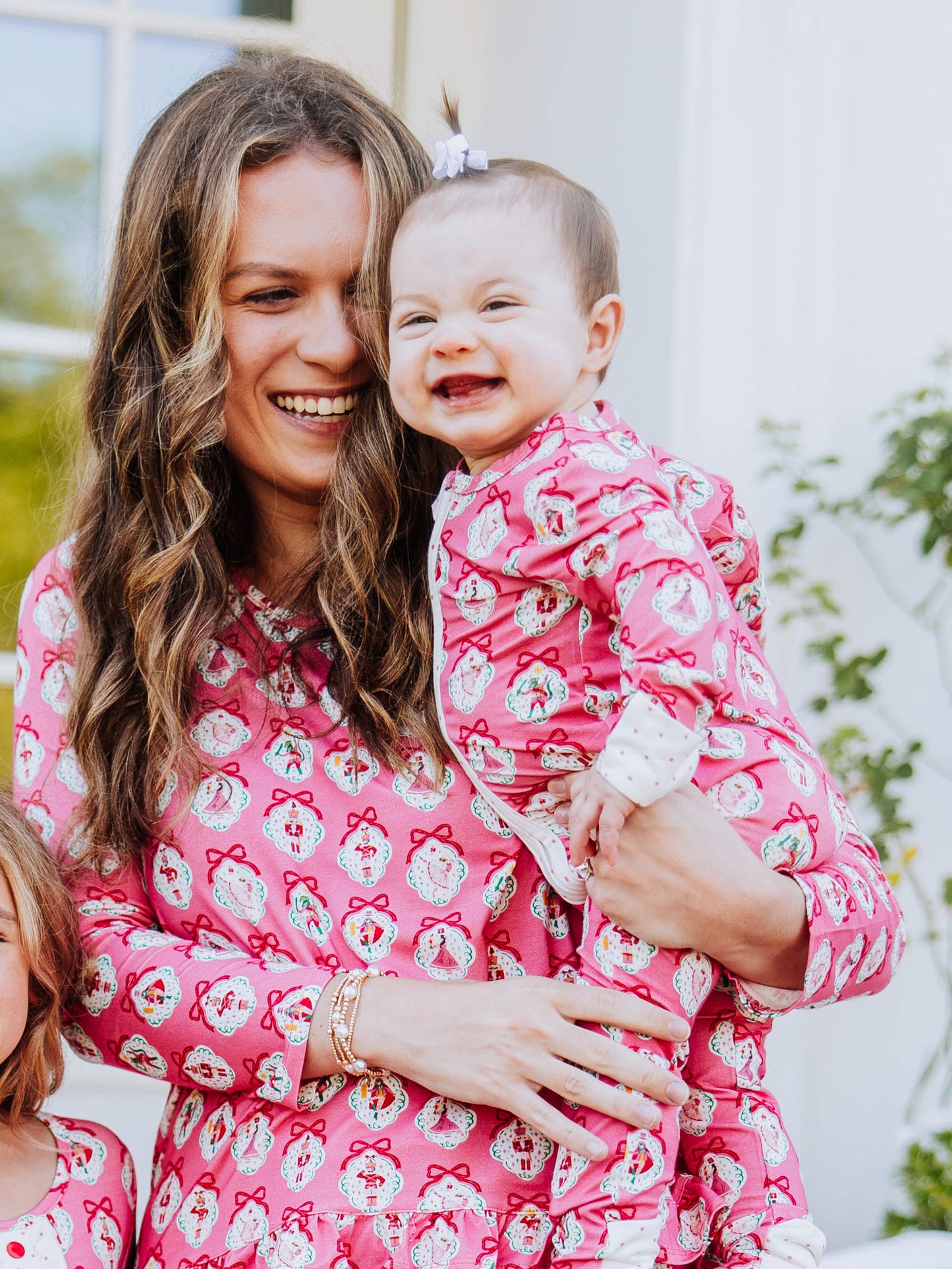 Mom holding baby and both are smiling and wearing the same printed pajamas. Print is pink nutcracker. 
