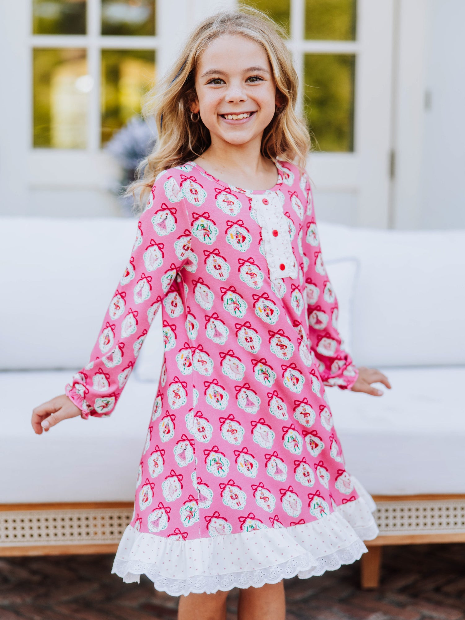 Girl standing outside on brick wearing a pink nutcracker printed dress. Model has hands to her side. 
