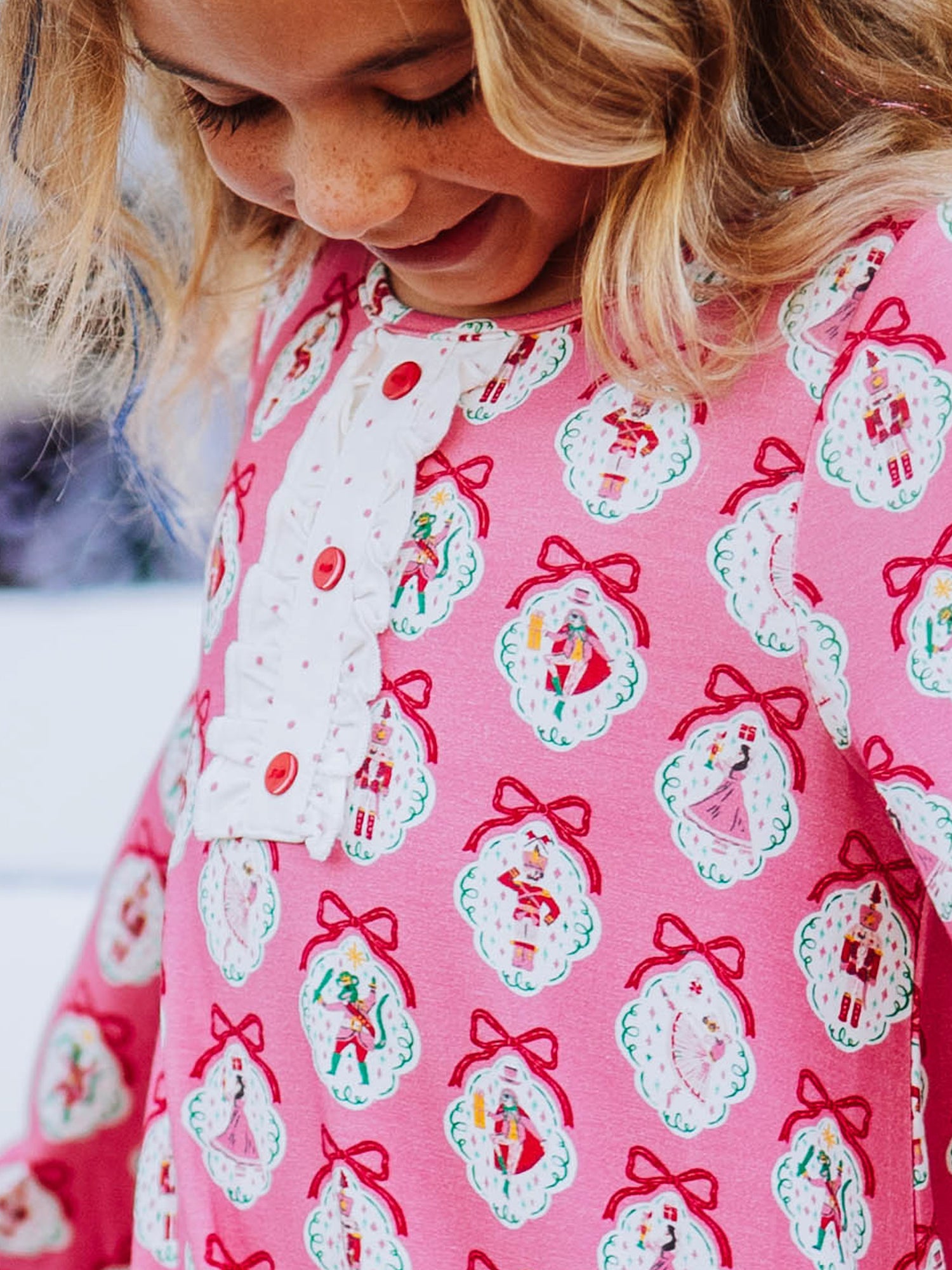 Close up of girl wearing a pink nutcracker printed dress and dress has a button trim on chest. 